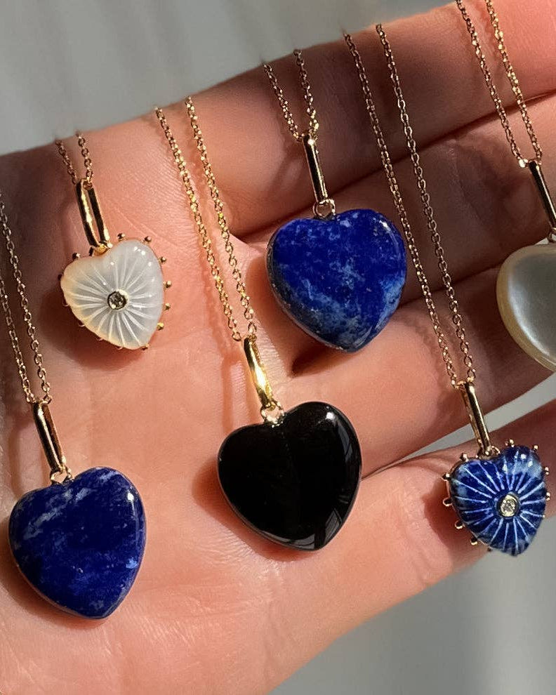 Heart-shaped stone pendants on gold chains held in a hand.