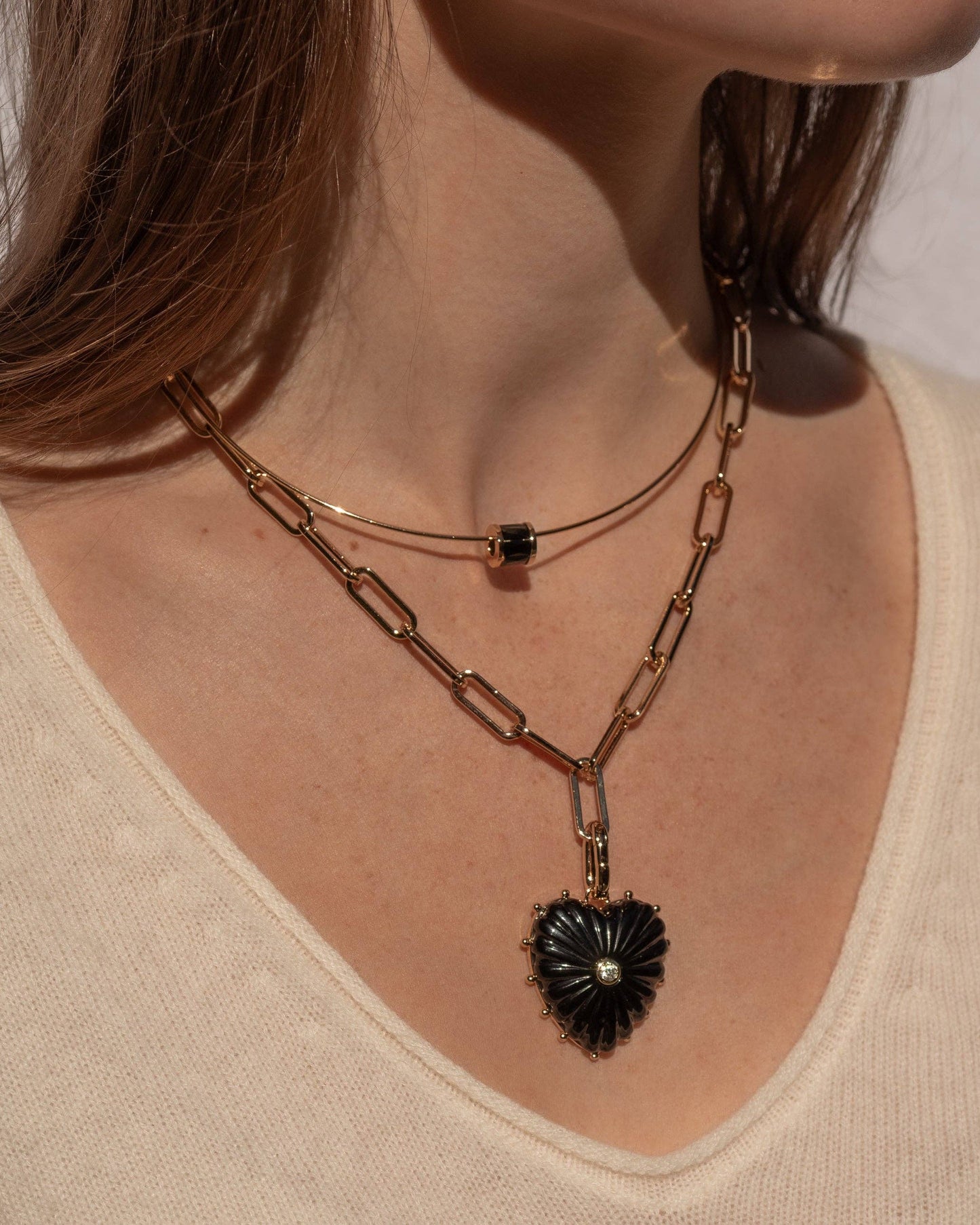 Close-up of a person wearing a gold chain necklace with a black pendant on a neutral background