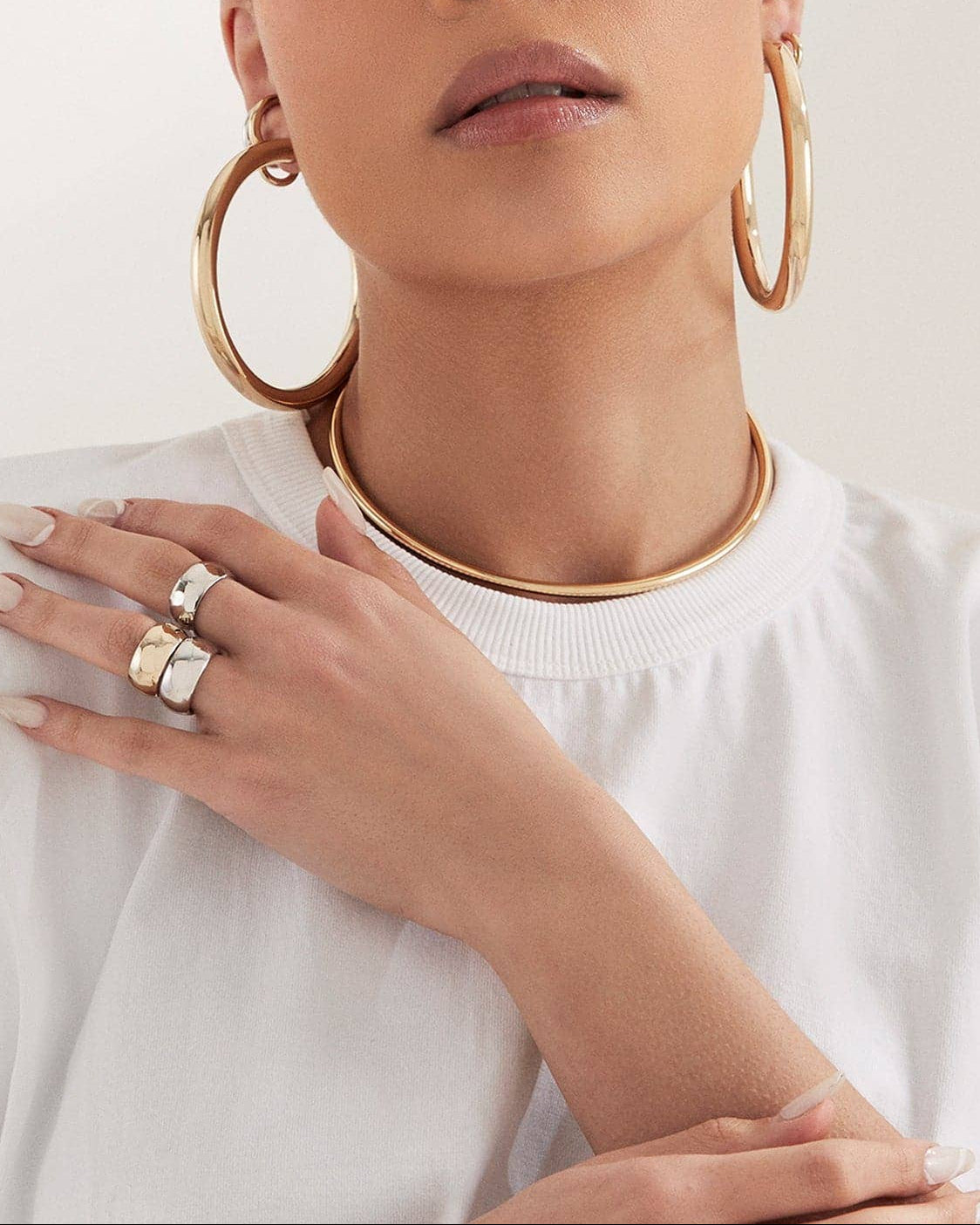 Woman wearing gold hoop earrings and rings on a white background