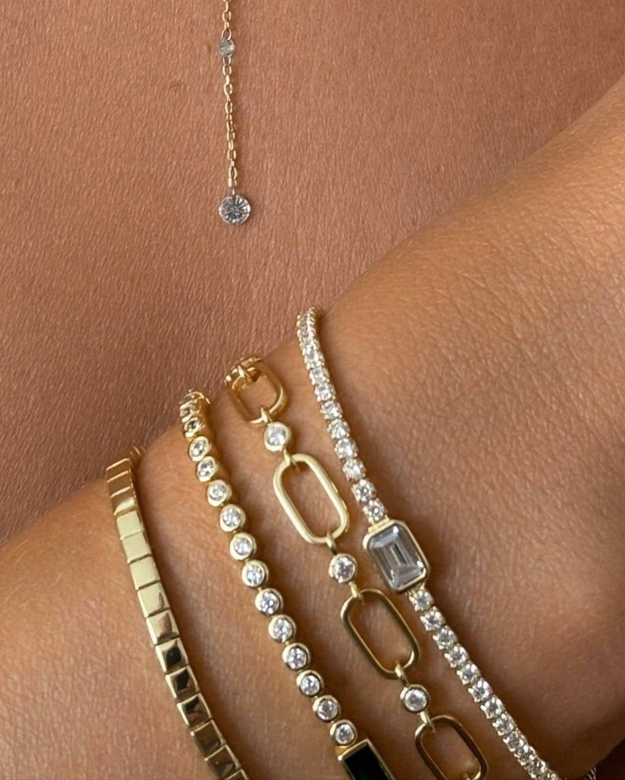 Gold jewelry set including a necklace and bracelets on a person's arm.