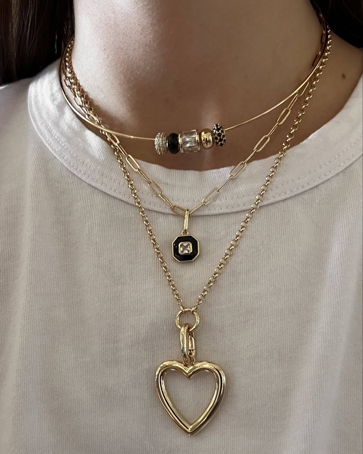 Person wearing multiple gold necklaces with heart pendants on a plain background