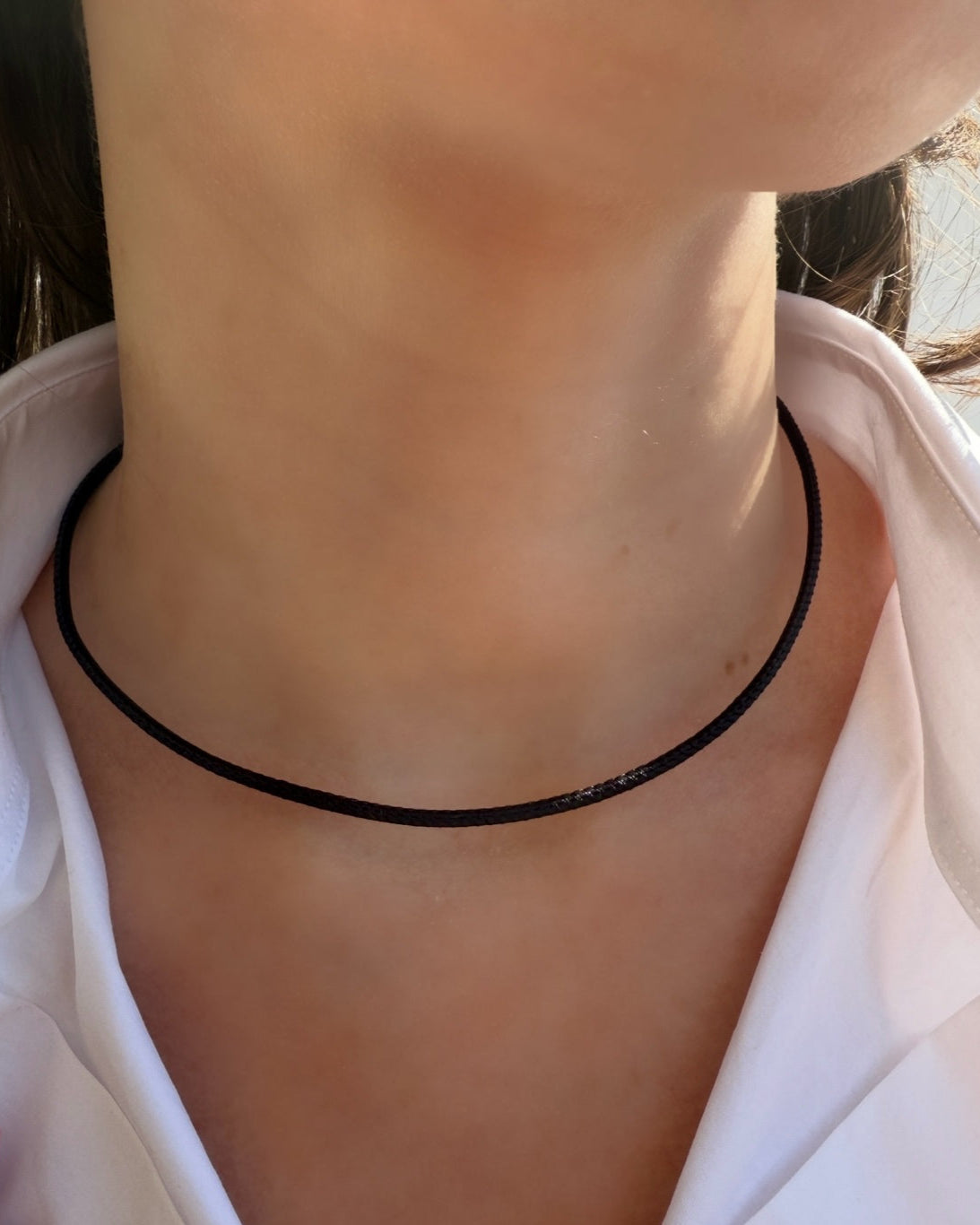 A close-up of a neck wearing the HANNAH Gold Leather Cord Necklace by Dylan James Jewelry/flower—a thin, adjustable piece, partially shown with a white shirt—ideal for minimalist jewelry lovers.