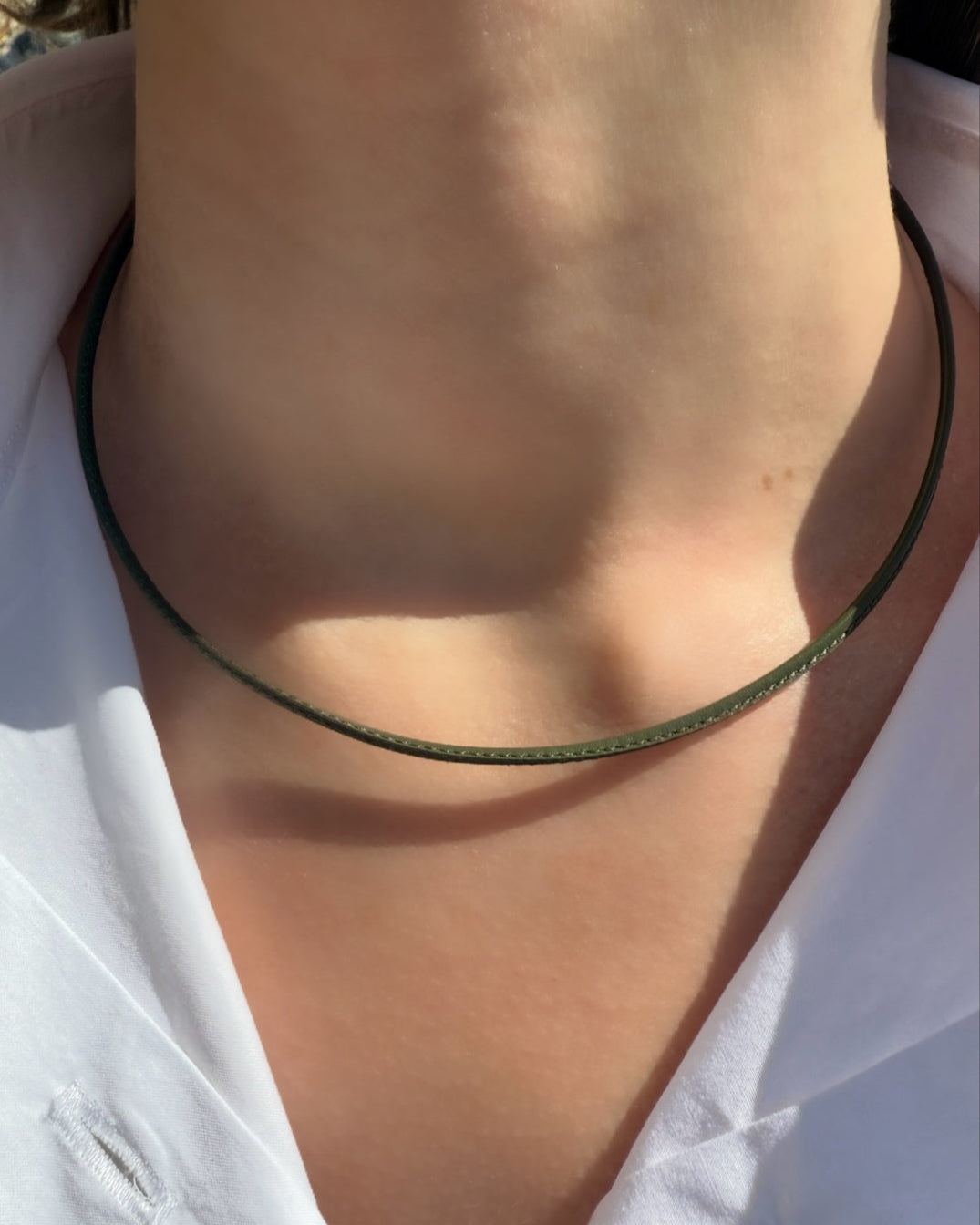 Close-up of a person's neck wearing the HANNAH Gold Leather Cord Necklace by Dylan James Jewelry/flower—a minimalist, thin choker—over a white collared shirt.