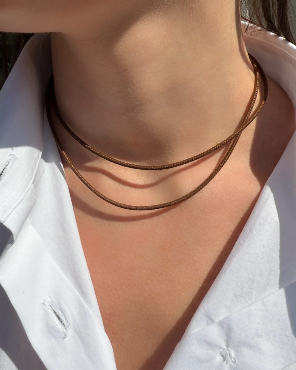 Close-up of a person wearing a white collared shirt and the HANNAH Gold Leather Cord Necklace by Dylan James Jewelry/flower, featuring minimalist style with adjustable layering for a modern look.