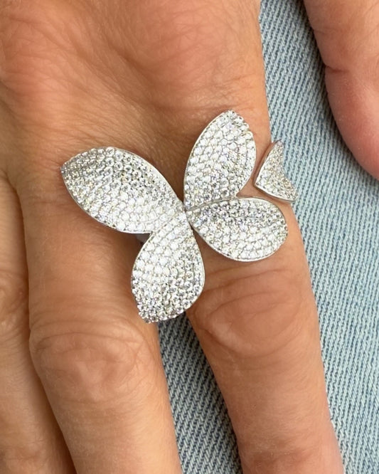 A close-up of a hand wearing the FLEUR Silver Diamond Ring by Dylan James, featuring CZ stone accents in a butterfly shape, set against a light denim background.