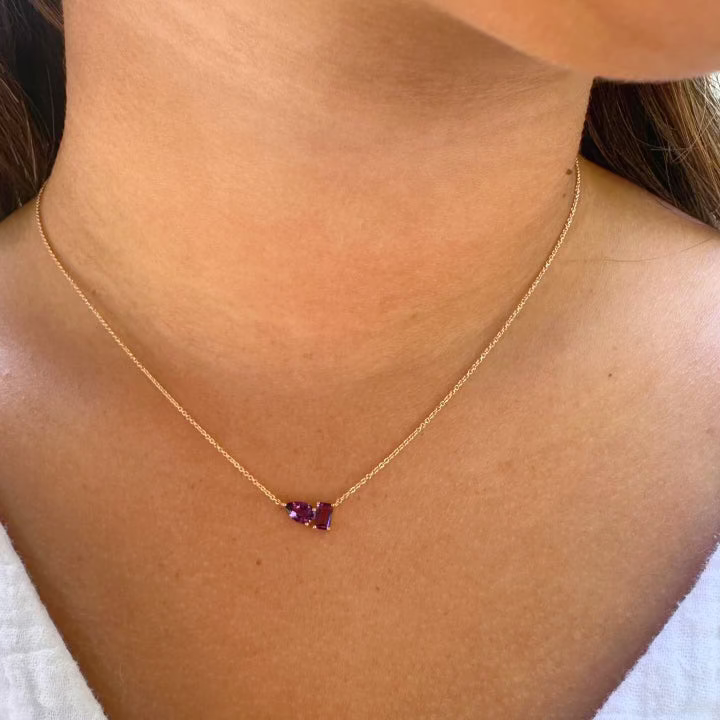 A person wears the AIRA BARNEY Amethyst Necklace, featuring a small amethyst pendant on a delicate 14kt yellow gold chain, shown against their neck and upper chest.