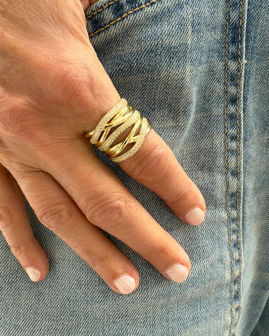 A hand with neatly manicured nails rests on denim jeans, adorned with the Dylan James NIC Gold Multi-Wrap Band Ring, showcasing its textured, multi-band design.