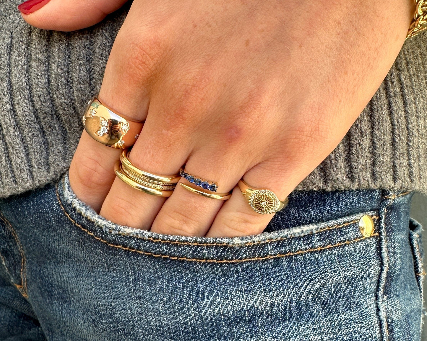 A hand adorned with Dylan James Jewelry's DEBBIE Diamond Ring rests in the front pocket of blue jeans. A sparkling diamond-studded bracelet glints on the wrist beneath the gray sweater sleeve.