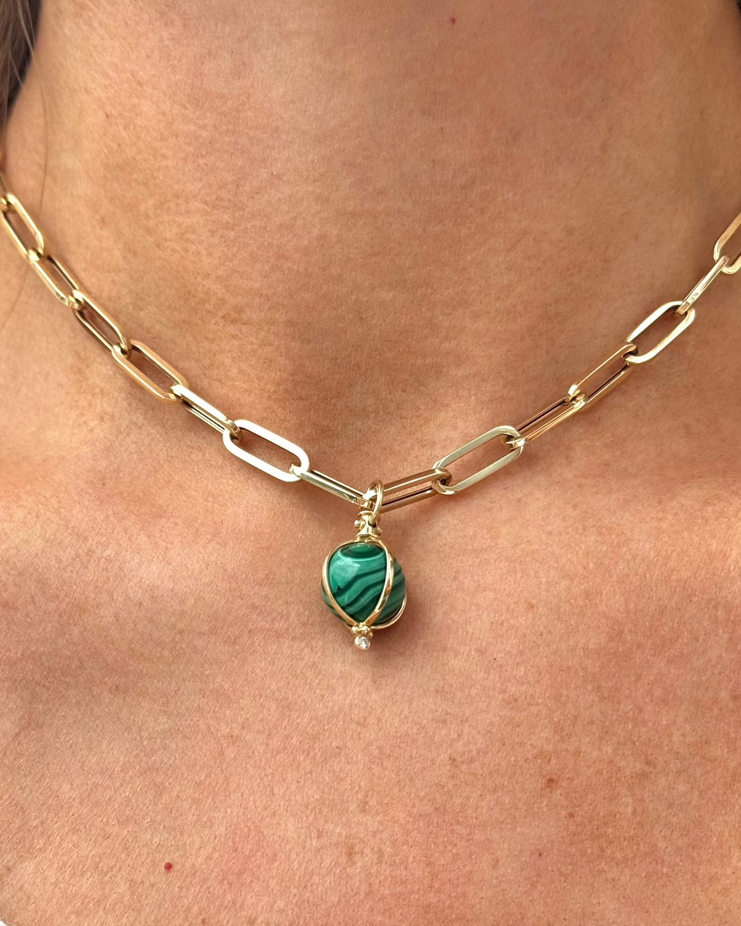 Close-up of a gold chain necklace with oblong links, featuring the ZENDA Malachite Necklace by Dylan James Jewelry, made of green malachite wrapped in 14kt yellow gold and adorned with a small diamond.