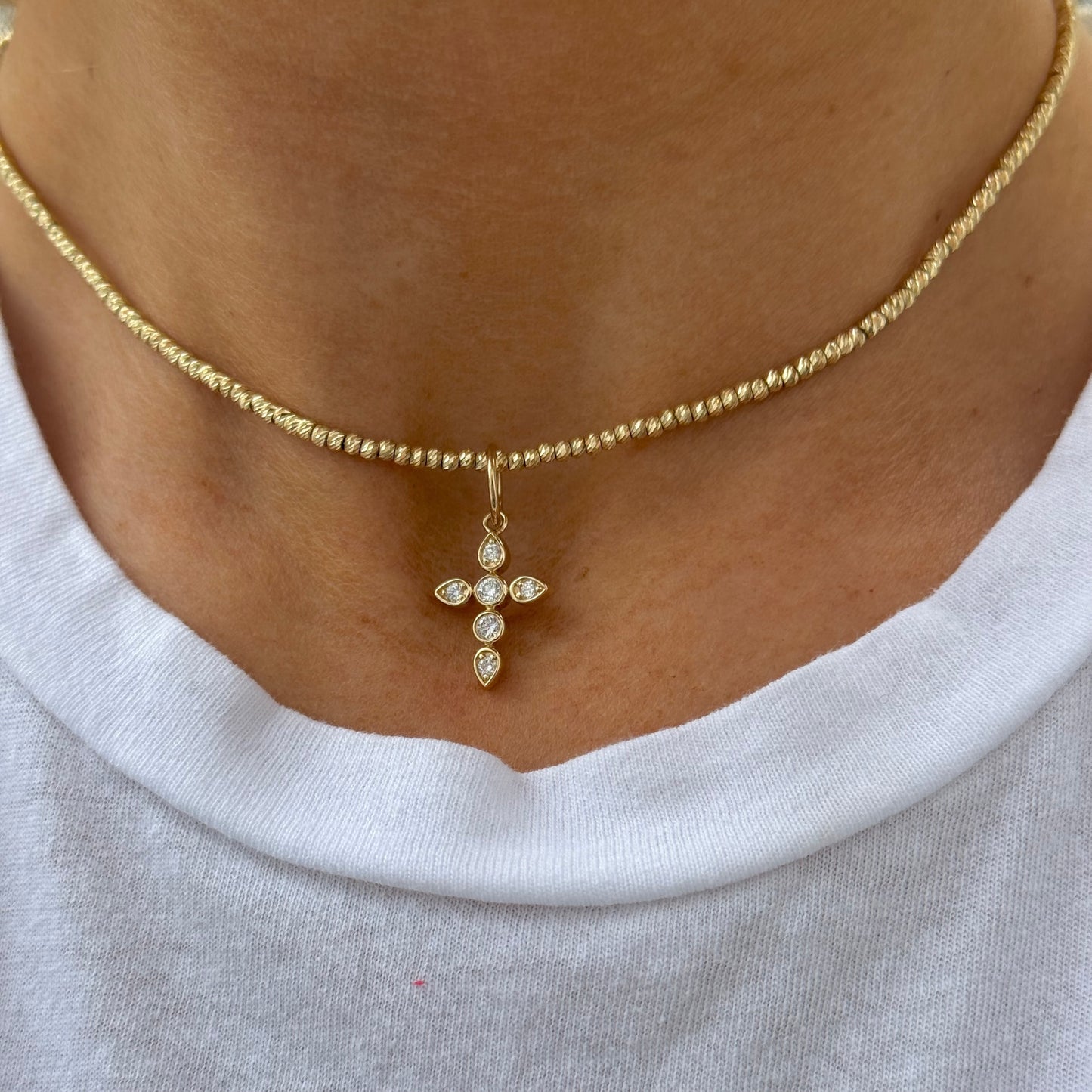 The aira "CISSY Gold Diamond Cross" necklace, featuring a yellow gold beaded design and diamond-studded cross pendant, elegantly complements a crisp white shirt.
