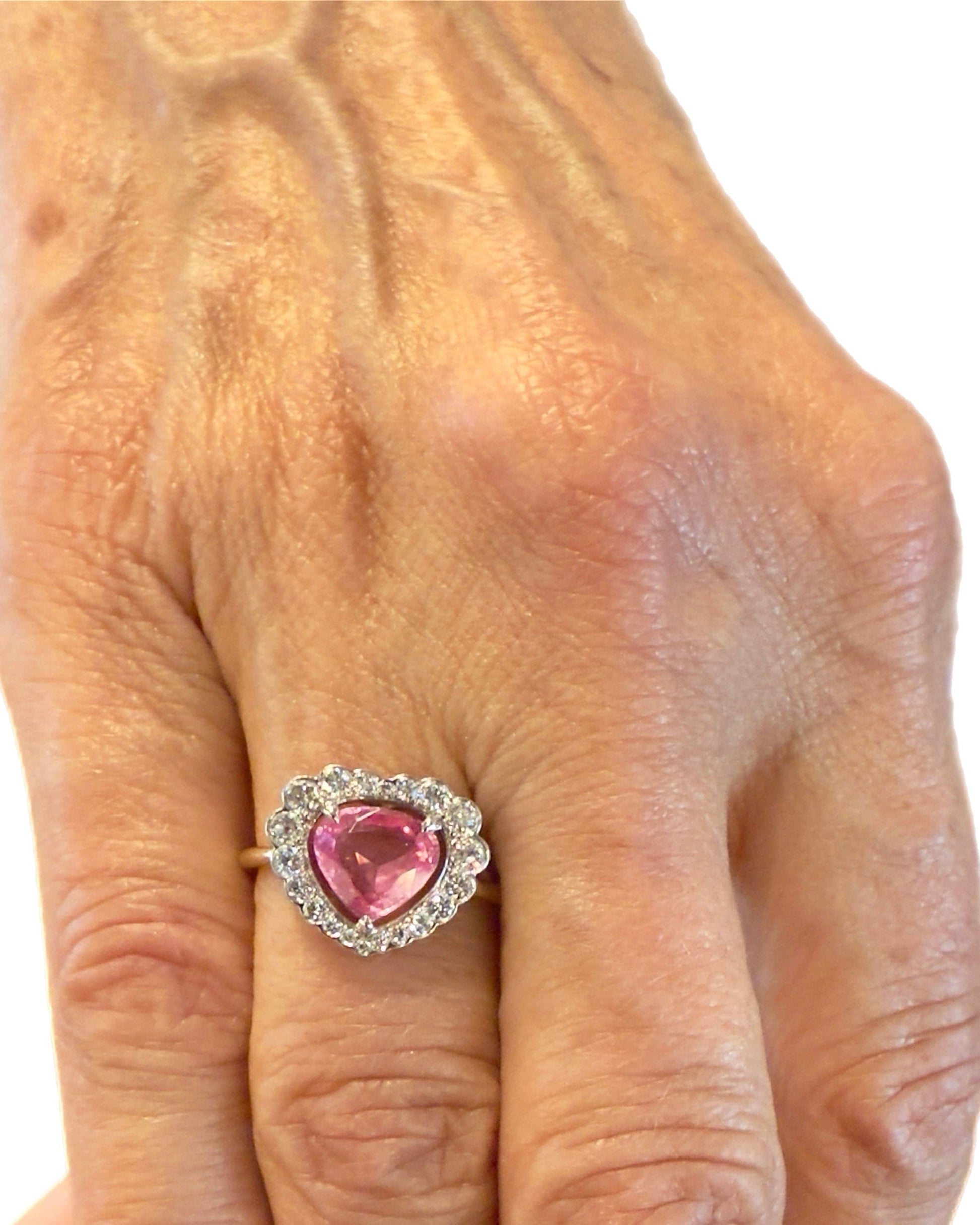 A hand wears the Dylan James NORA KOGAN Vintage Diamond Spinel Ring—featuring a heart-shaped Mahenge pink spinel and clear accents—on the ring finger, displayed against a white background.