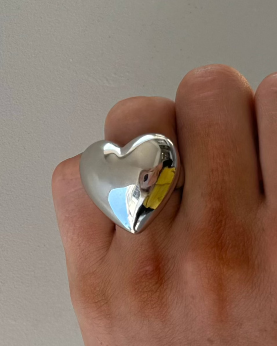 A hand wearing the NOAH Silver Chunky Ring by Dylan James Jewelry, its shiny surface reflecting a person dressed in yellow.