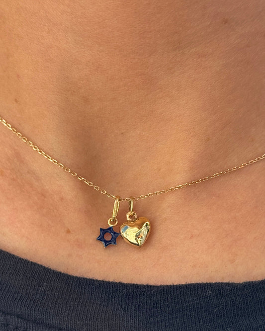 Gold necklace with two charms worn by a person against a dark background