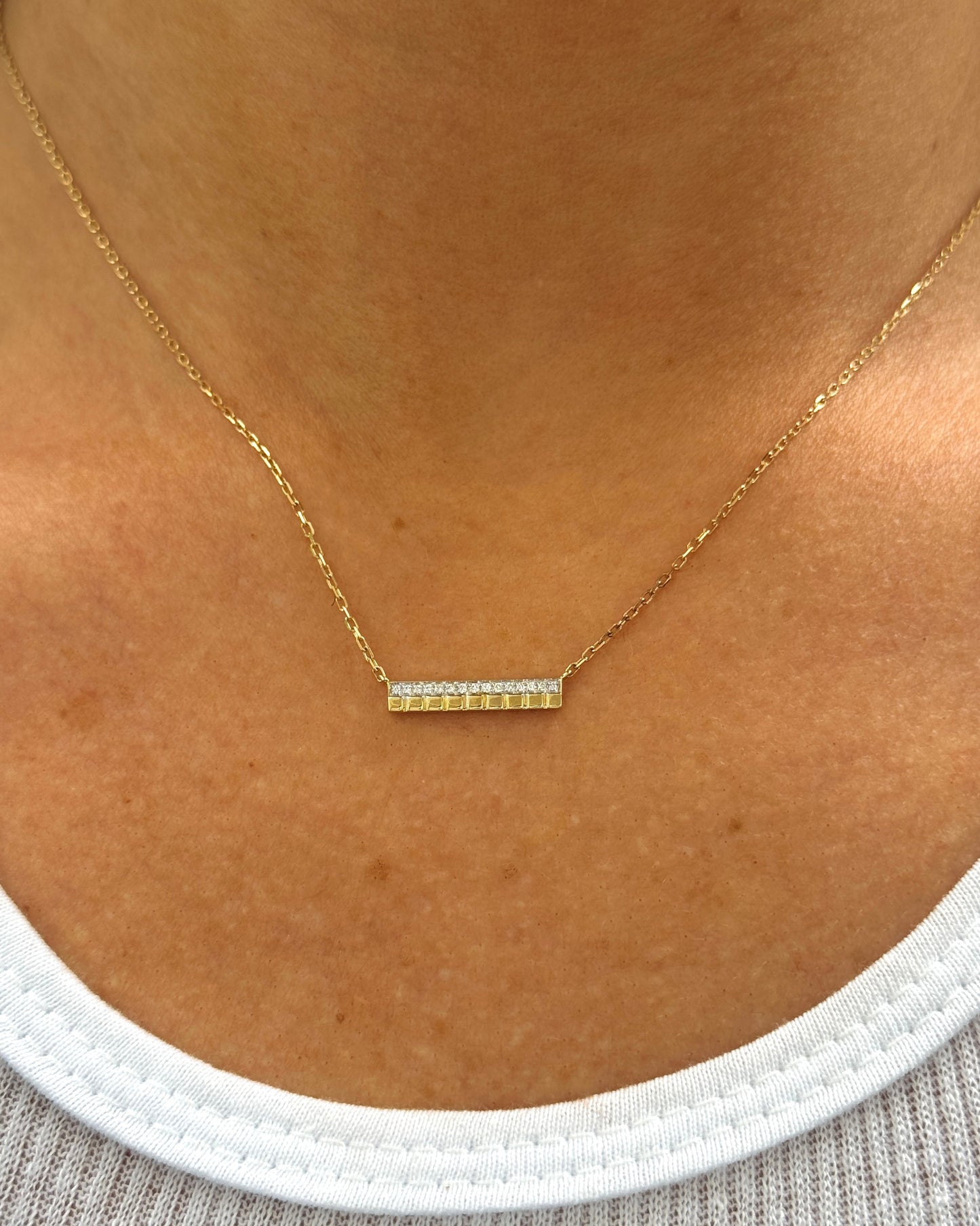 Gold necklace with a bar pendant on a person's neck