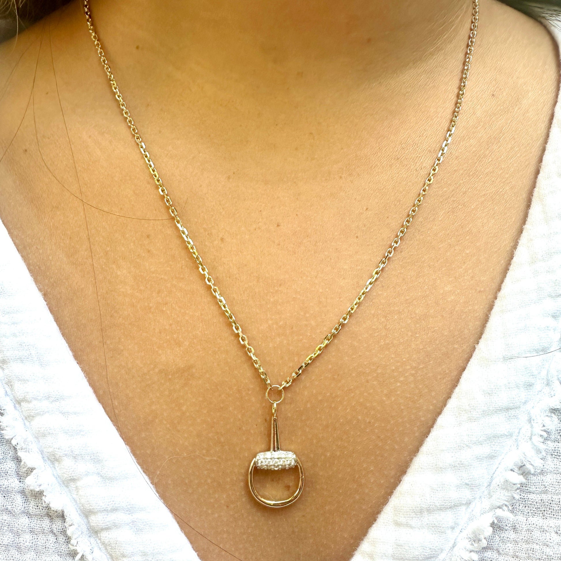 The BUD Gold Diamond Necklace by AIRA is a stunning 14kt yellow gold piece featuring a circular pendant adorned with sparkling gems and diamonds, elegantly worn against a light-colored textured top.