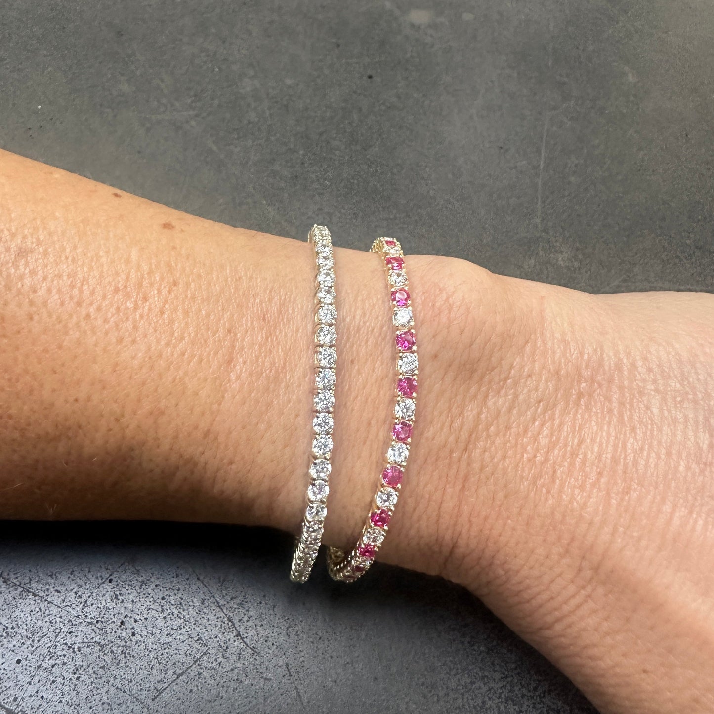 Two bracelets on a wrist: the DANI Tennis Bracelet with clear Cubic Zirconia stones, and another with pink stones, both crafted by dylan james jewelry in 925 Sterling Silver, exuding GEORGE elegance.