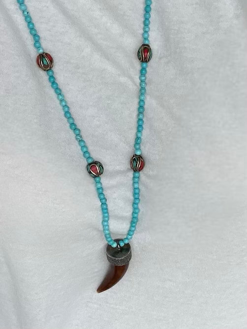 The JOE turquoise Beaded Necklace by Dylan James Jewelry, featuring inlay accent beads and a claw-like brown pendant, is styled over a white shirt.