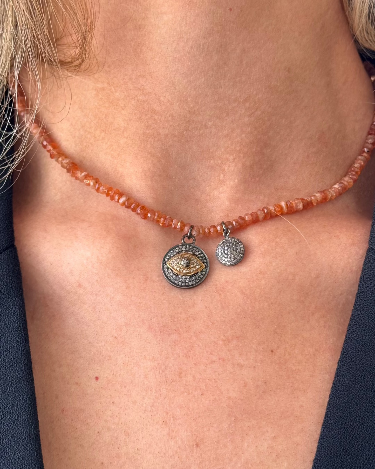A person wearing the MOOD Stone Diamond Necklace by Dylan James Jewelry, featuring chunky red beads with two round silver pendants and delicate gold accents, shown close-up against a black top.