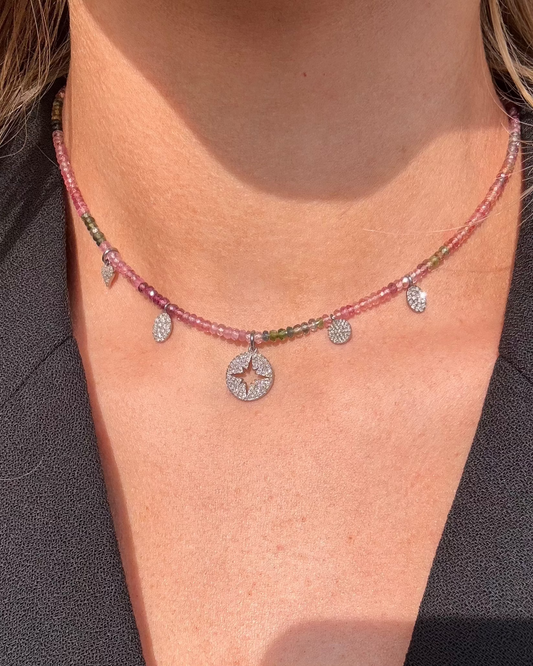 A woman showcases the MATHIAS Tourmaline Diamond Charm Necklace by Dylan James Jewelry, a multi-colored creation with tourmaline beads and circular and teardrop pendants, elegantly set against a black top.