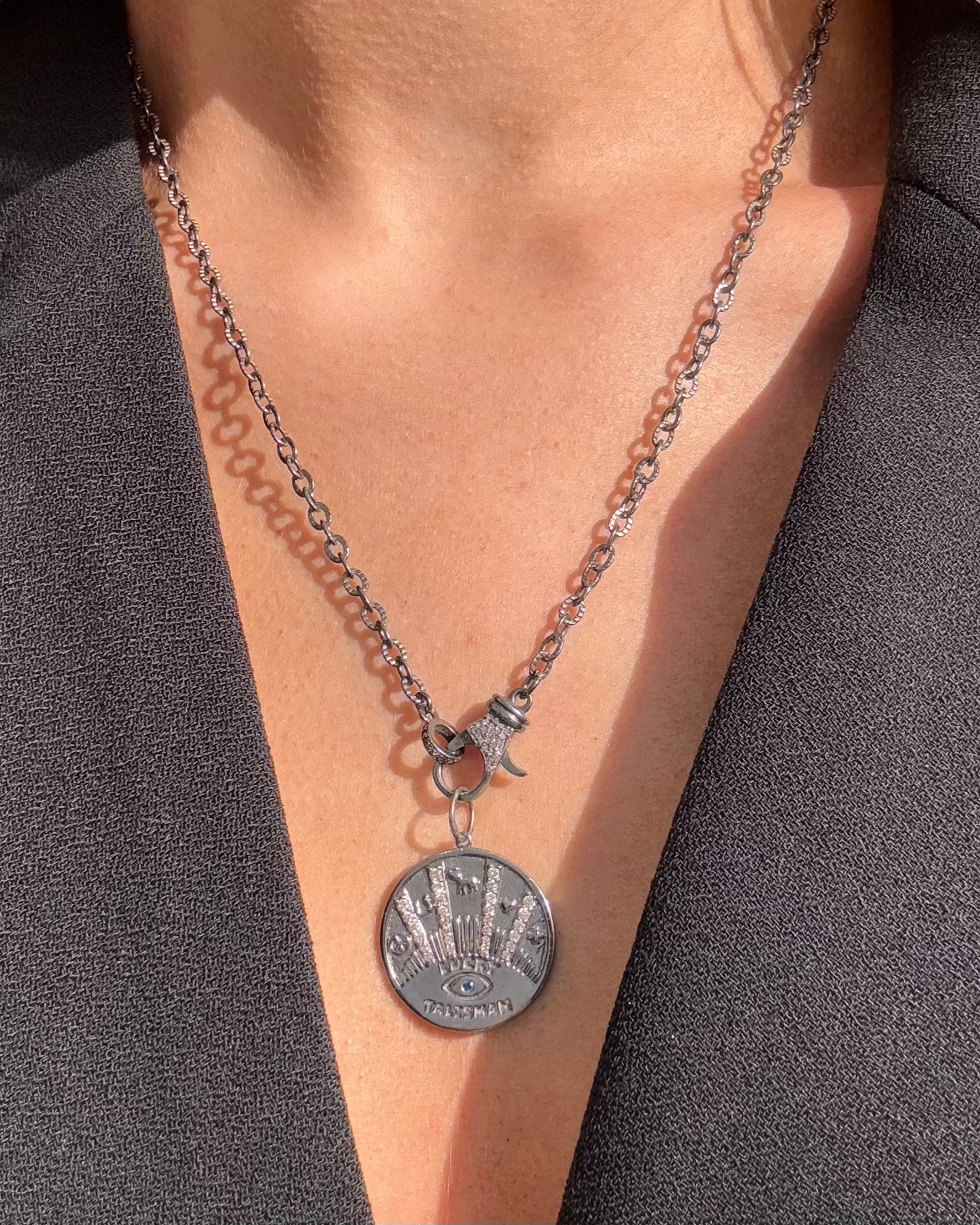 A person adorned with the TALISMAN Silver Diamond Necklace from Dylan James Jewelry, showcasing an eye-shaped lucky talisman design, elegantly draped over a black V-neck top.