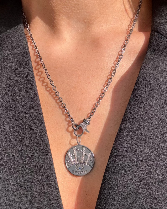 A person adorned with the TALISMAN Silver Diamond Necklace from Dylan James Jewelry, showcasing an eye-shaped lucky talisman design, elegantly draped over a black V-neck top.