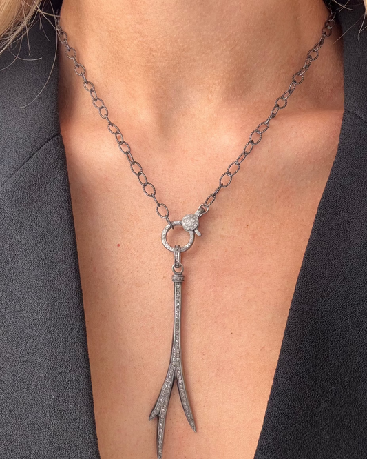 A person wearing a black blazer and the MICA Silver Diamond Necklace by Dylan James Jewelry, featuring an abstract pendant on a 26" oxidized silver chain.
