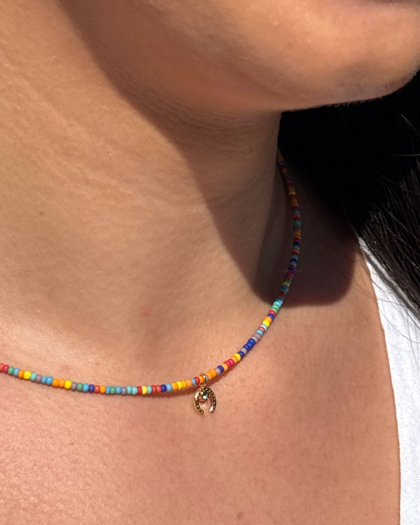 Close-up of a colorful beaded necklace with a gold charm on a person's neck.