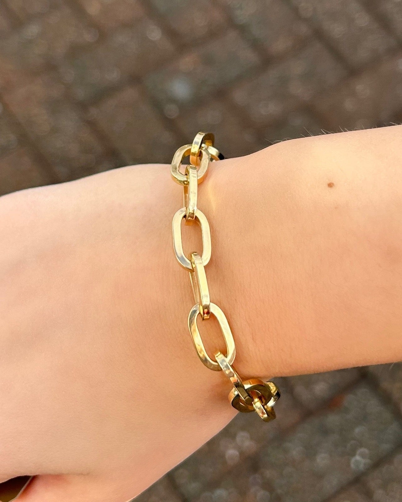 Gold chain bracelet on a wrist with a blurred brick pavement background