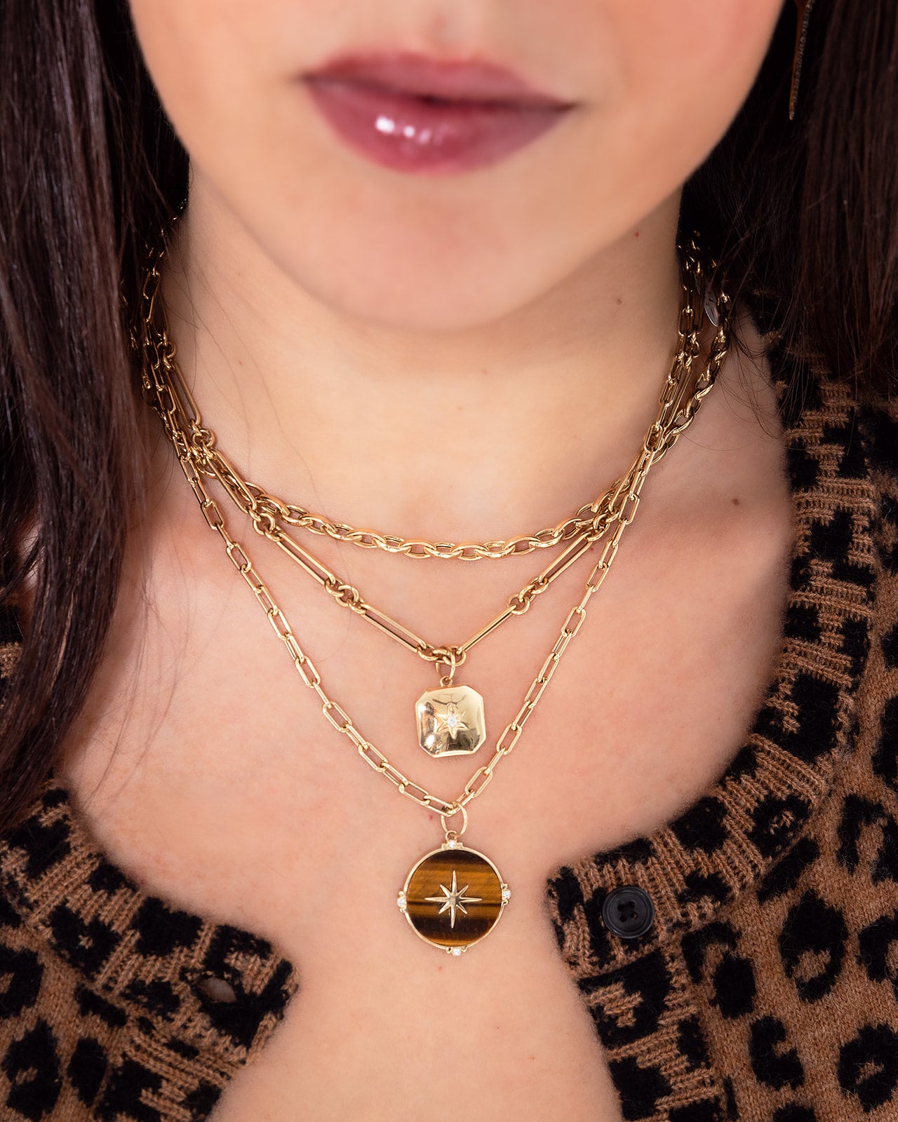 A close-up features layered ANNIE Gold Chain necklaces by AIRA, including an eye-catching 16" version with extender, flaunting pendants with a round star design that perfectly complements a patterned brown top.