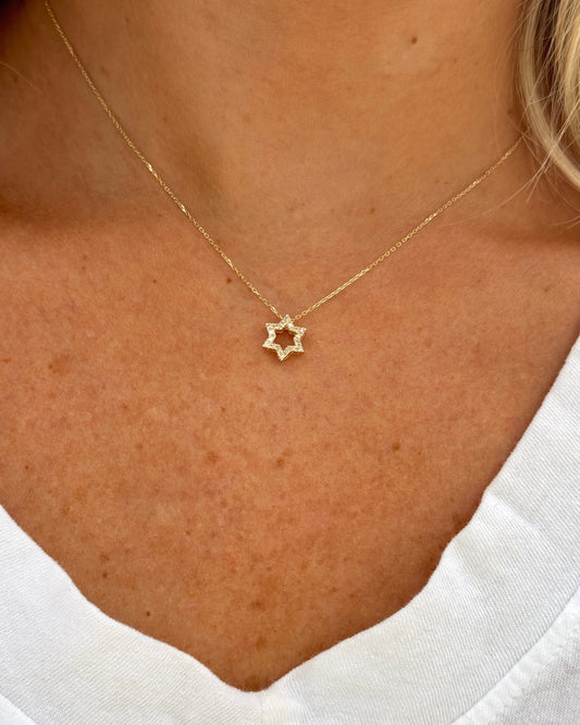 A close-up of a person wearing the Dylan James BEN gold diamond star necklace and a white V-neck shirt.