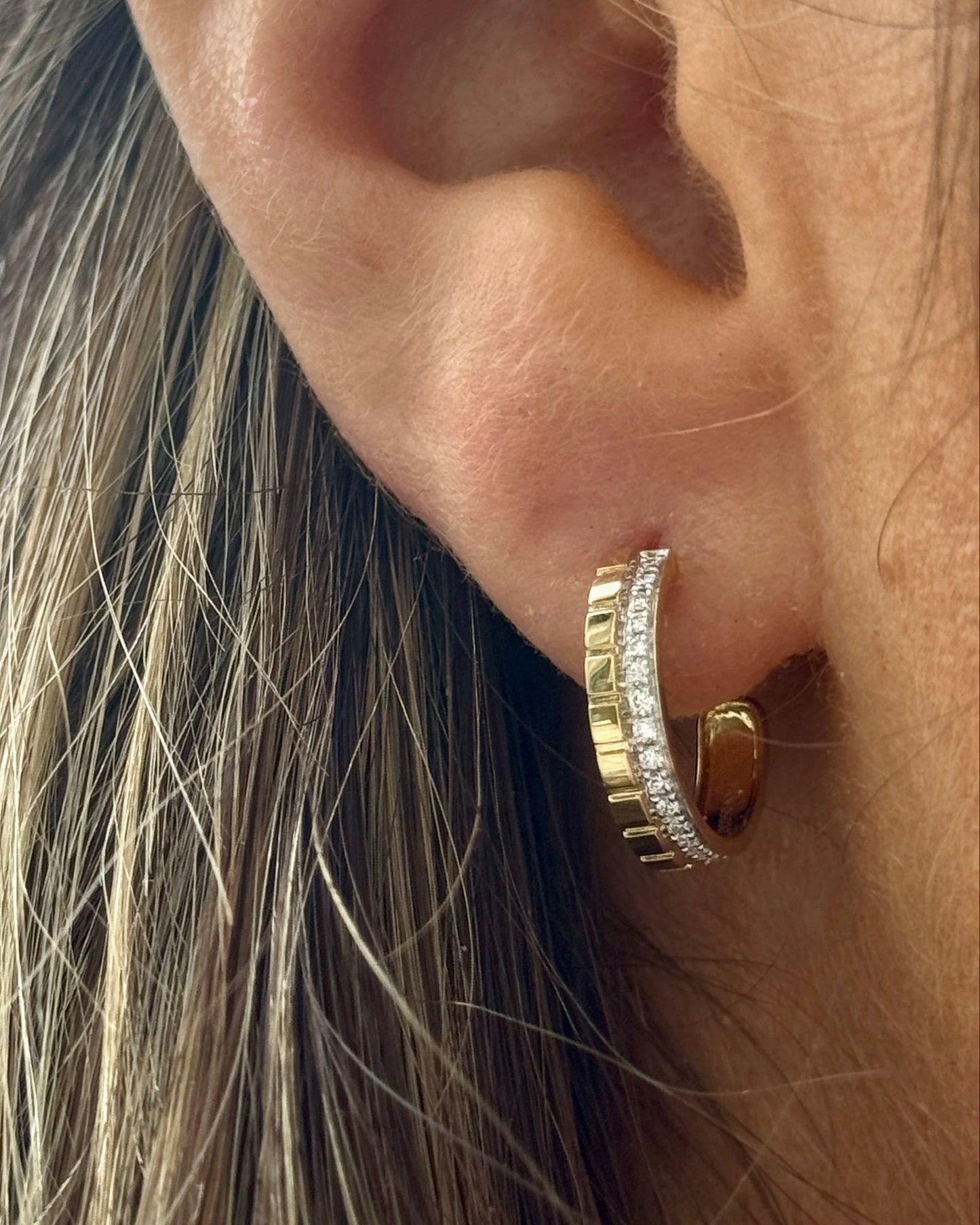 Close-up of an ear wearing a gold hoop earring with a blurred background