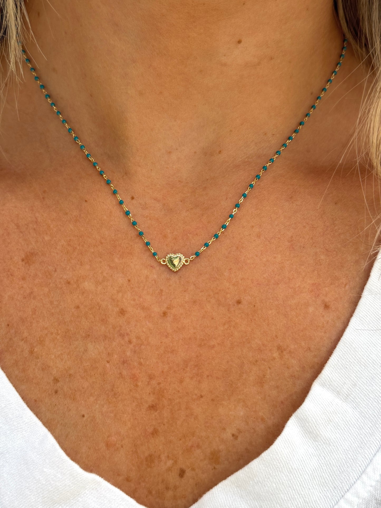Necklace with a heart-shaped pendant on a person wearing a white shirt.