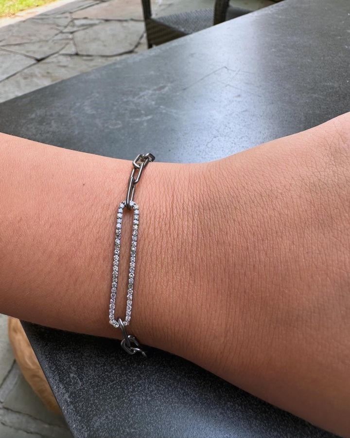 The GIGI Diamond Bracelet by Dylan James Jewelry, crafted in sterling silver with a rectangular rhinestone-encrusted centerpiece, elegantly adorns a person's wrist over a dark table surface.