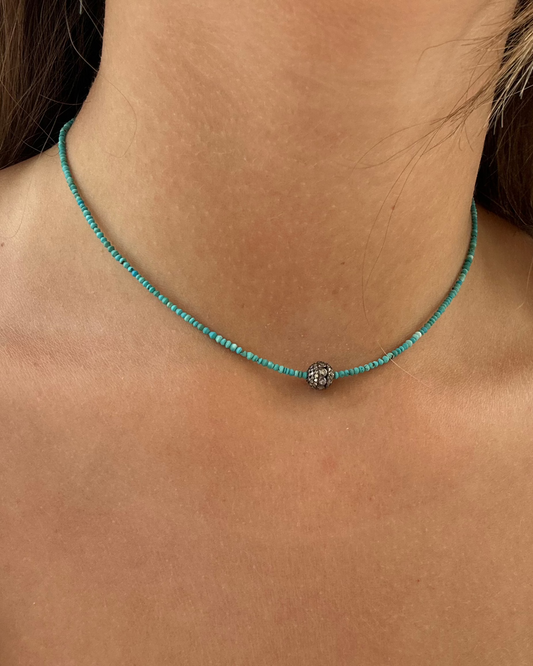A close-up of a person's neck wearing the Dylan James ZAC Turquoise Diamond Bead Necklace, featuring minimalist style with thin turquoise beads and a central small silver decorative bead.