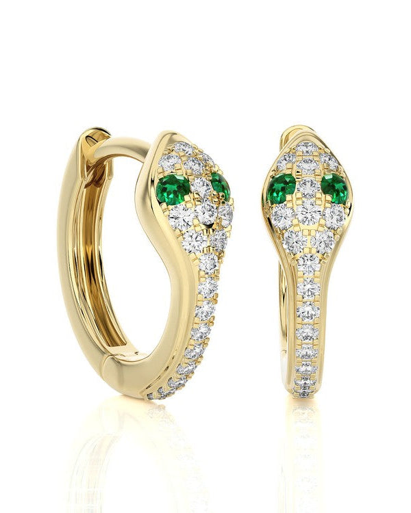 A pair of gold huggie hoop earrings with pavé-set clear stones and green emerald-cut accents, shown on a clean white background with a soft reflection.