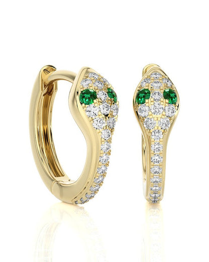 A pair of gold huggie hoop earrings with pavé-set clear stones and green emerald-cut accents, shown on a clean white background with a soft reflection.