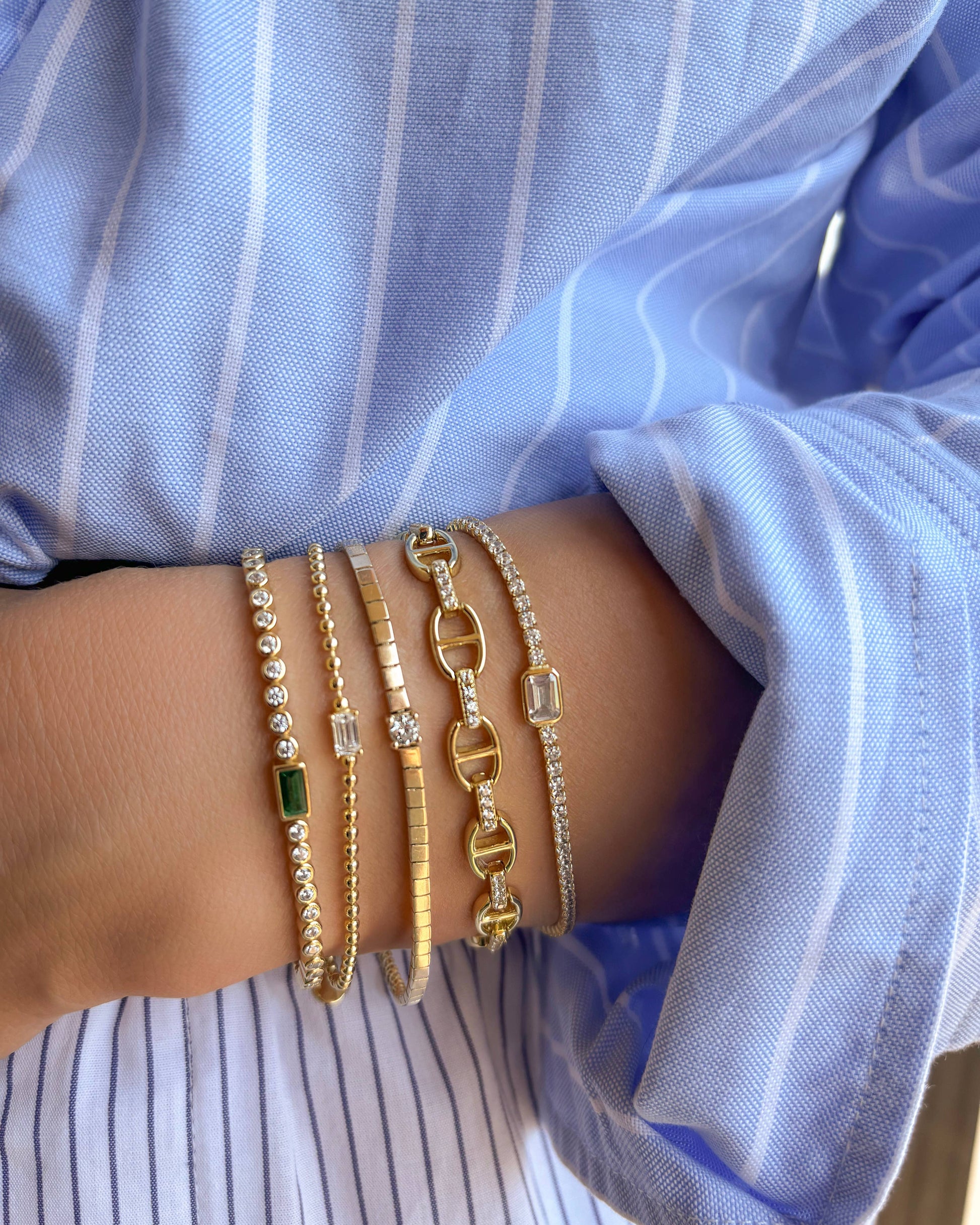 Close-up of a wrist wearing multiple gold bracelets with a blue shirt in the background