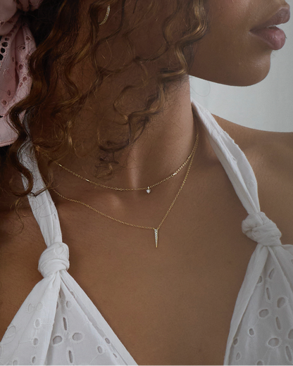 Woman wearing a pink headscarf and white top against a white curtain background