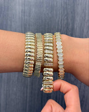 A close-up of a person's wrist and hand wearing five stacked metallic bangles against a blue-gray textured background.