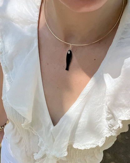 Person wearing a white blouse with a deep neckline and a gold necklace with a black pendant.