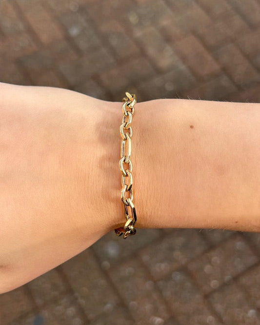 Gold chain bracelet on a wrist with a blurred brick background
