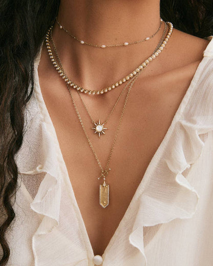 Close-up of a woman wearing multiple gold necklaces with a white blouse.