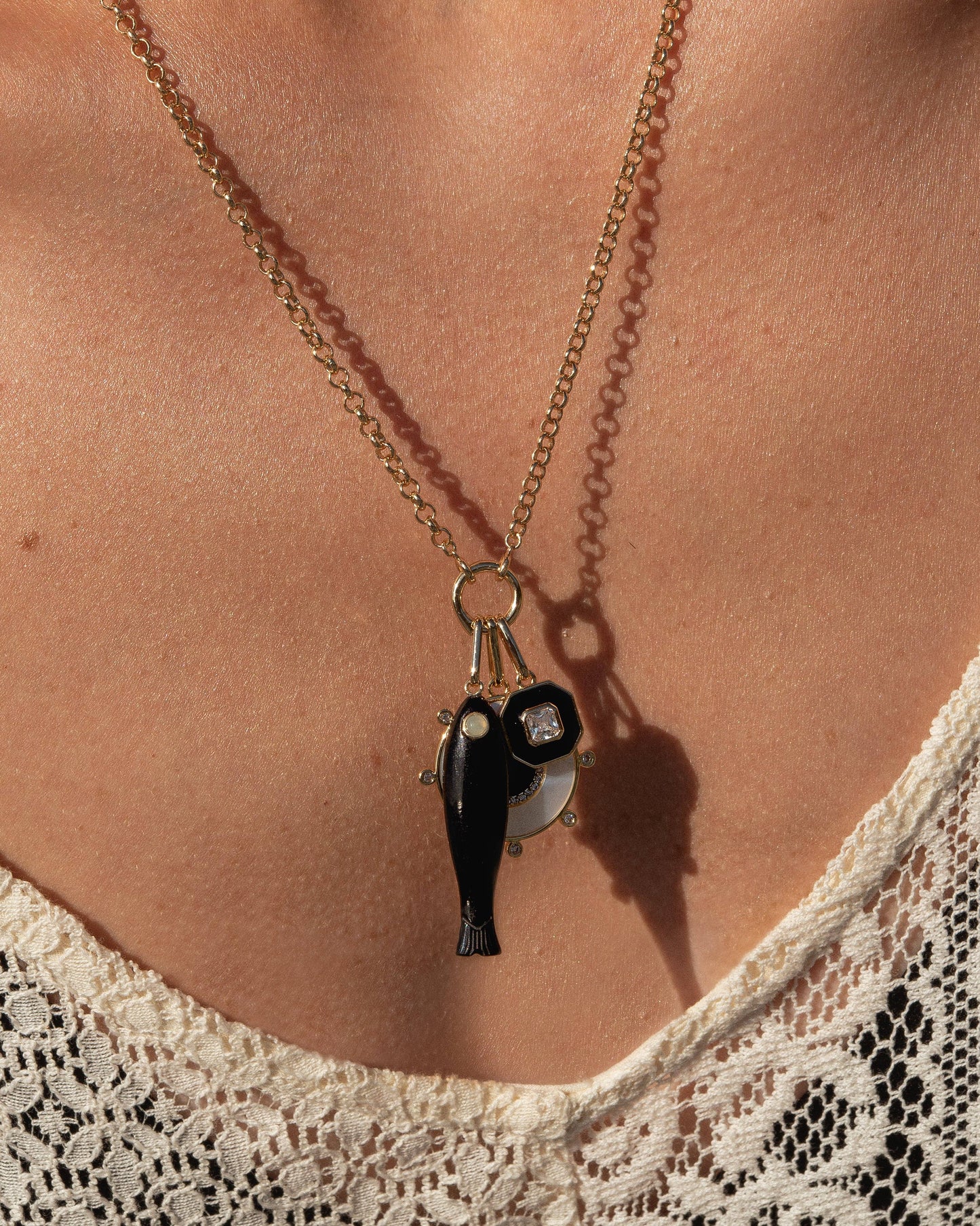 Necklace with a pendant featuring a fish and a bird on a person wearing a lace top.