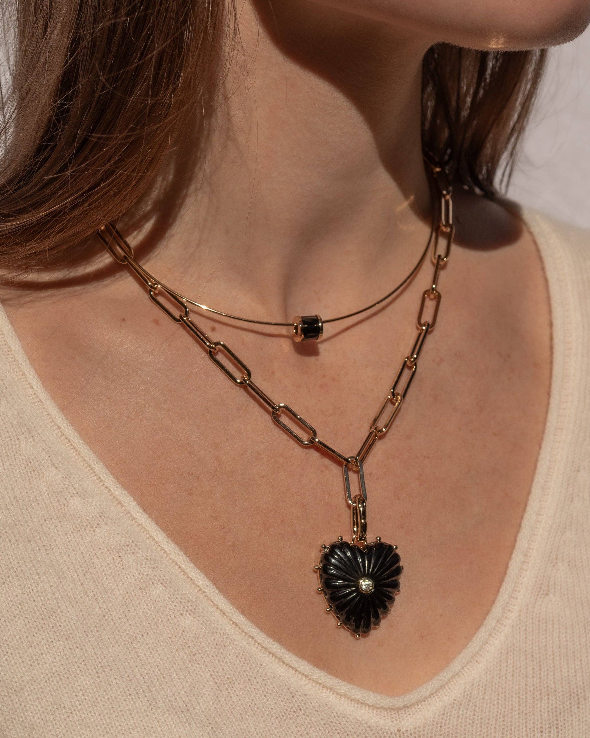 Close-up of a person wearing a gold chain necklace with a black pendant on a neutral background