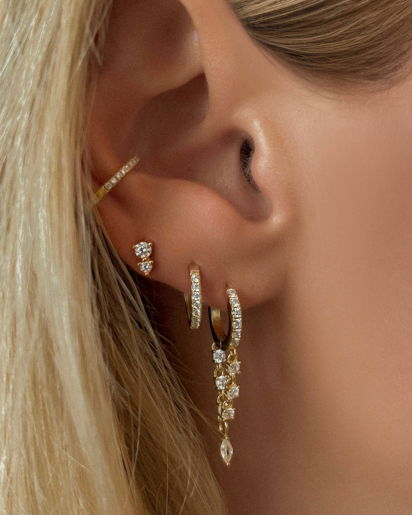 Close-up of an ear with gold hoop earrings and a dangling earring.