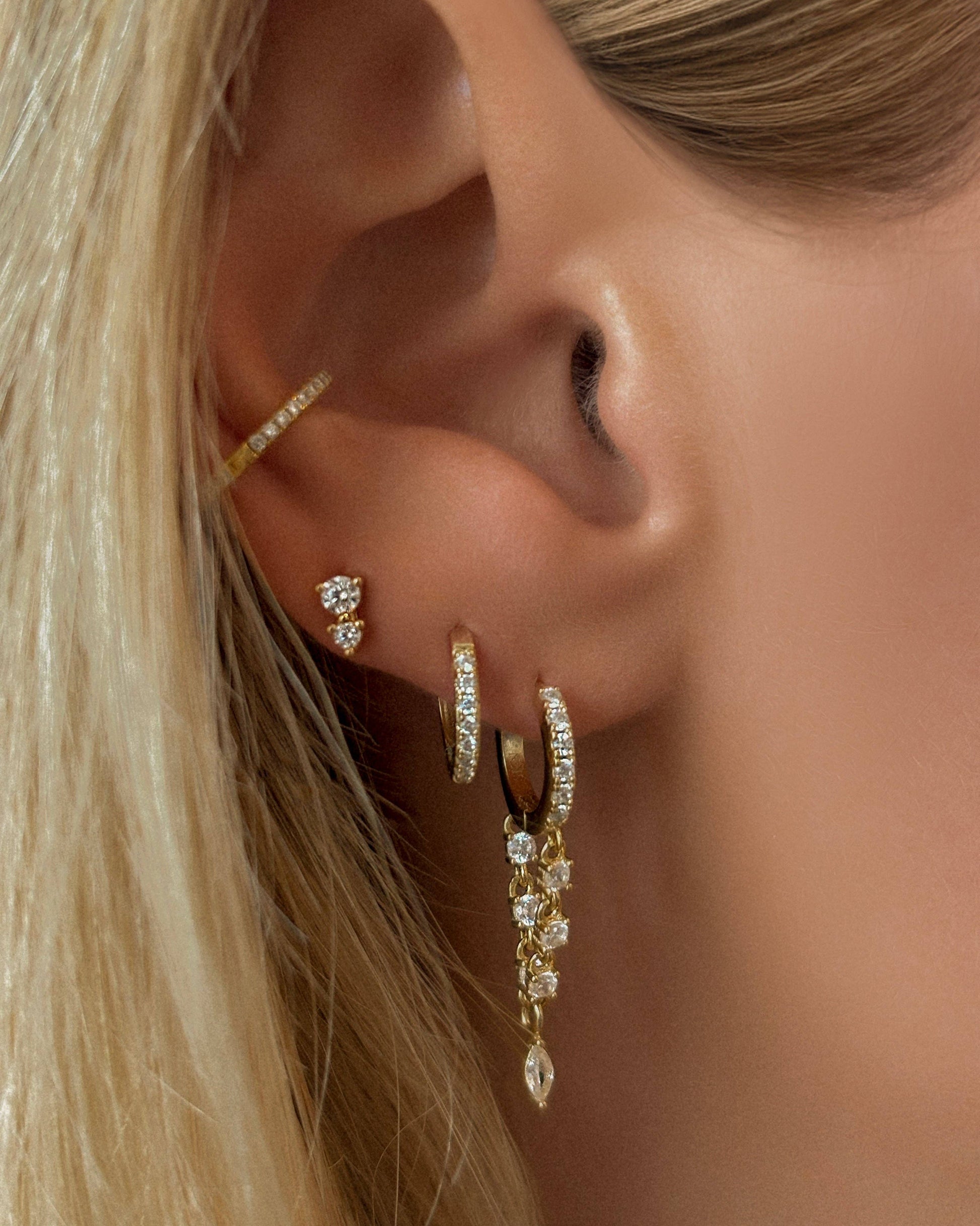 Close-up of an ear with gold hoop earrings and a dangling earring.