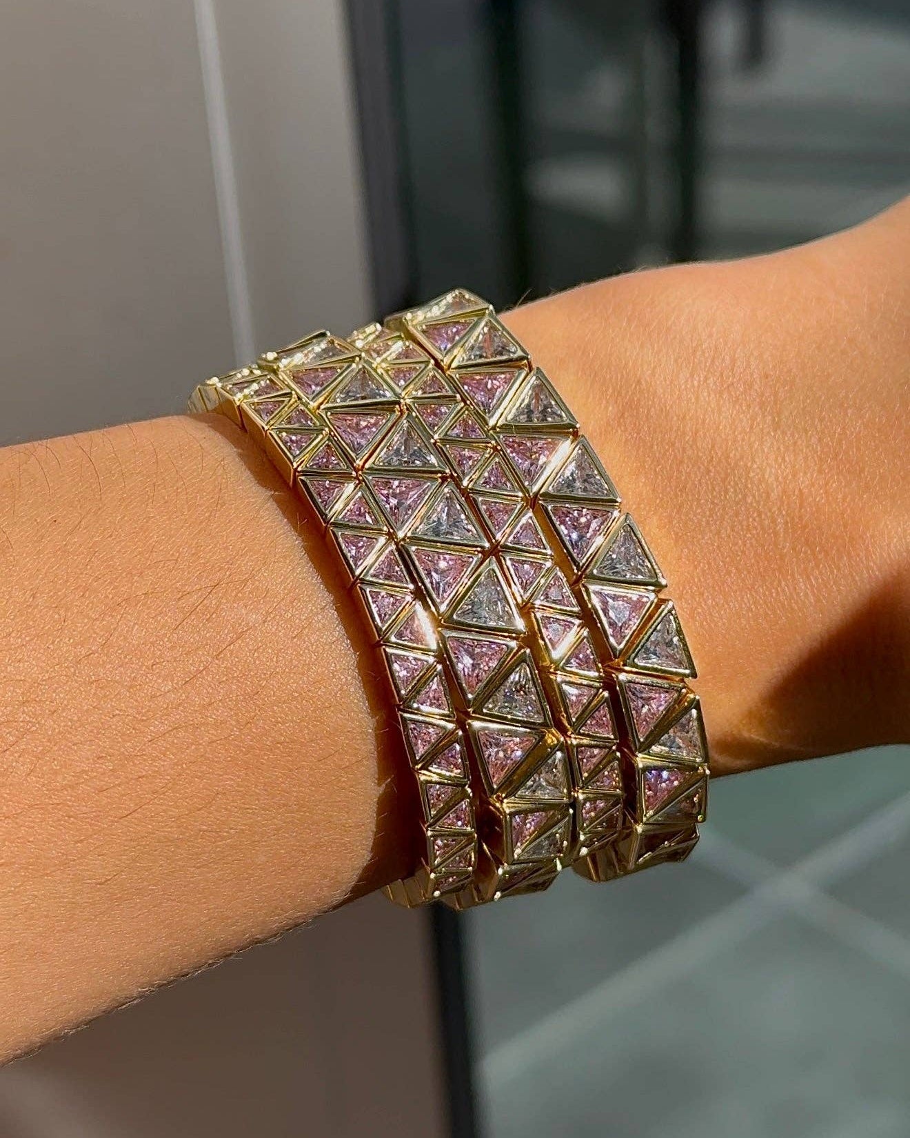 A close-up of a gold-toned multi-band cuff bracelet with pyramid-shaped crystal-encrusted panels, worn on a person's wrist.