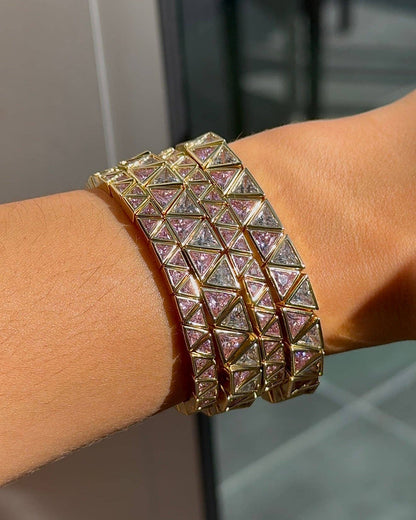 A close-up of a gold-toned multi-band cuff bracelet with pyramid-shaped crystal-encrusted panels, worn on a person's wrist.