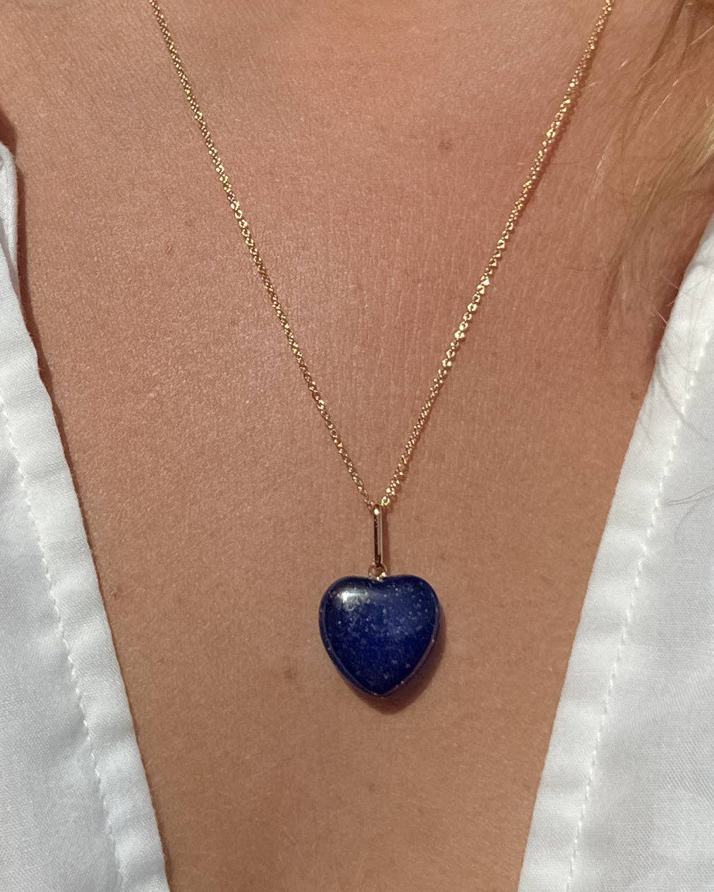 Gold necklace with a blue heart pendant on a person wearing a white shirt.