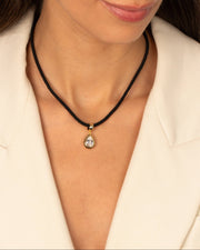 Person wearing a black beaded necklace with a gold pendant